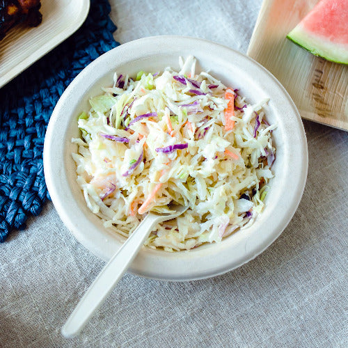 A 16oz compostable bowls of coleslaw and a plate of watermelon on a table