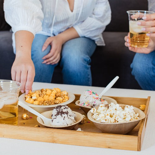 Two women sitting on a couch with a Bamboo Serving Tray of food