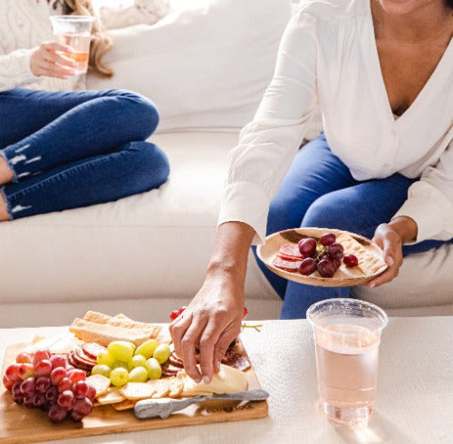 Two women enjoying a meal on a couch with a tray of food on eco-friendly palm leaf plates.